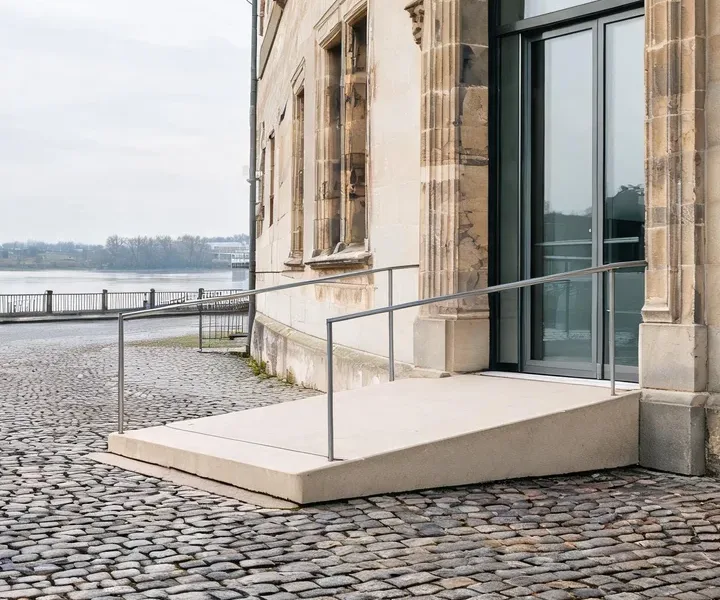 Eingang der Kanzlei in einem sanierten Sandsteinhaus: gläserne Tür, davor eine Rampe mit Handlauf auf Kopfsteinpflaster
