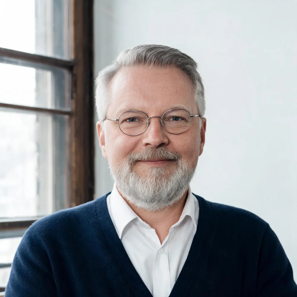 Porträt von Rechtsanwalt Tilo Lesche mit grauem Bart, runder Brille und dunkelblauer Strickjacke vor einem Altbaufenster